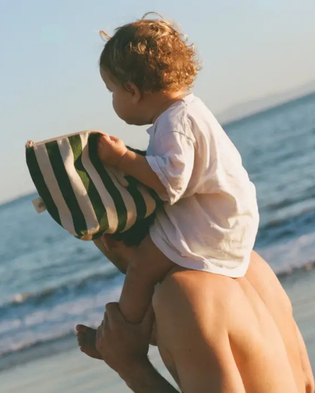 Person holding a child on a beach with a striped bag
