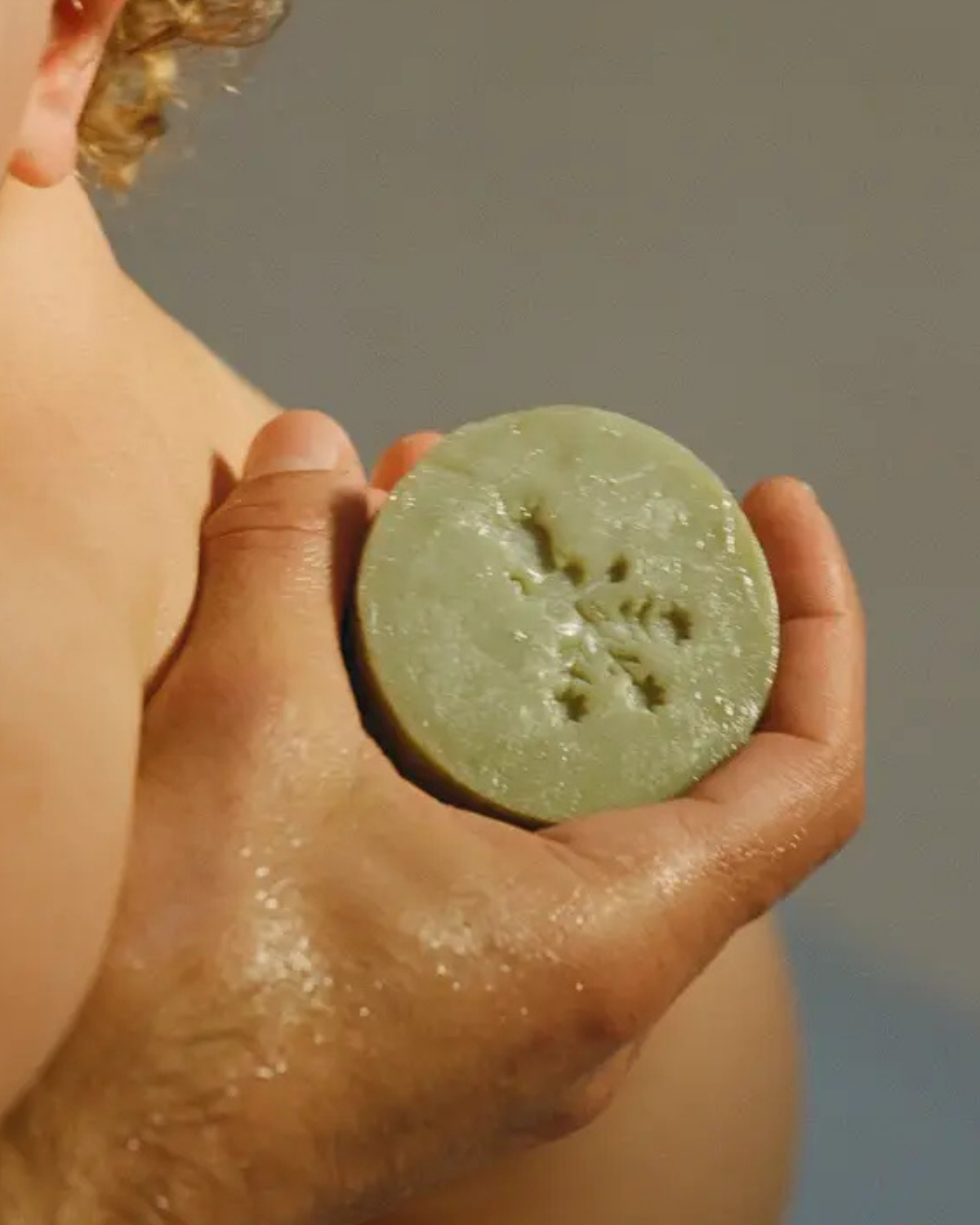 Hand holding a green bar of soap against a neutral background