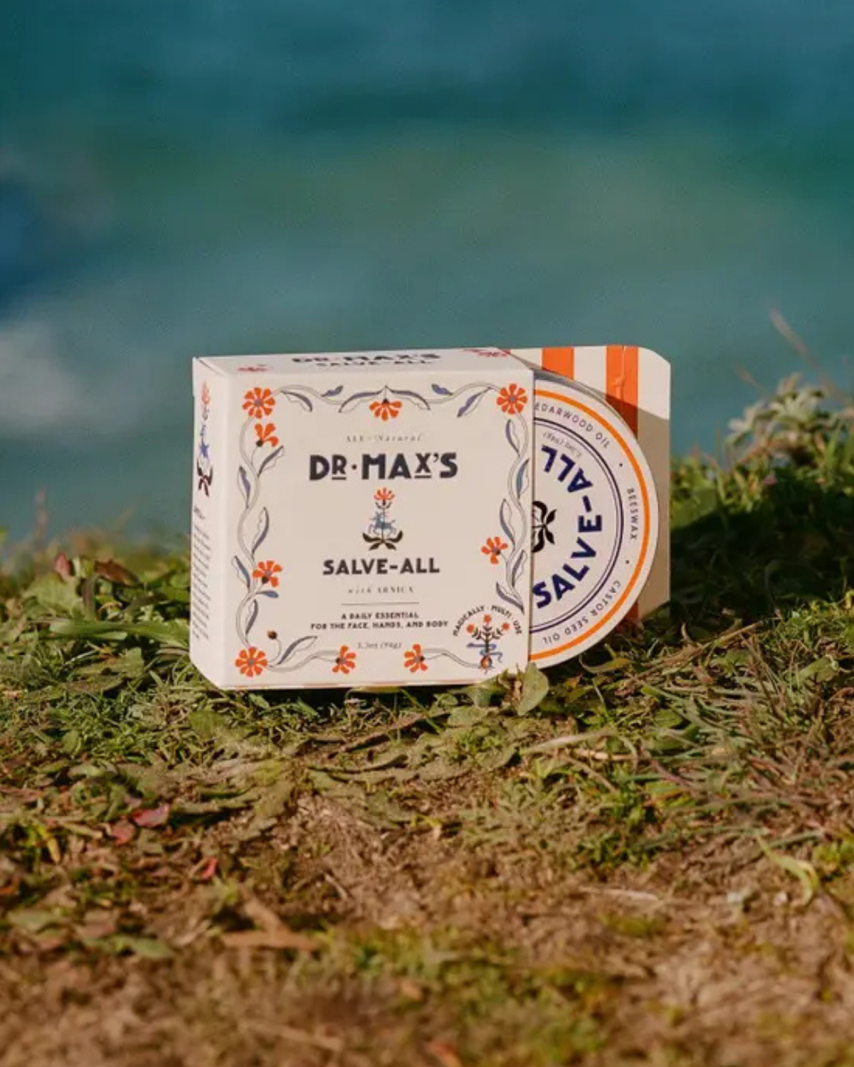 Dr. Max's Salve packaging on grass with a blurred natural background