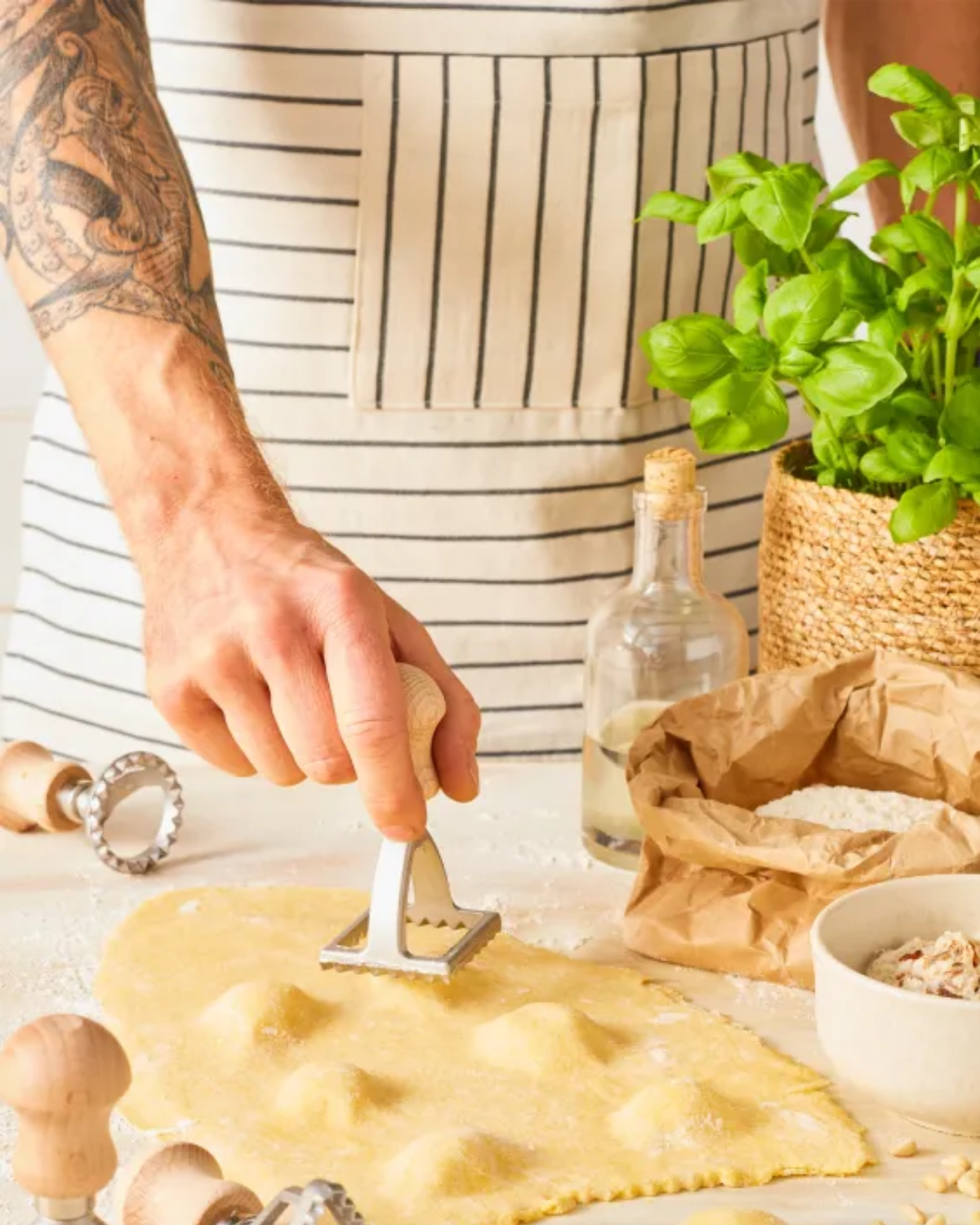 Person making pasta with a tool on a kitchen counter, surrounded by ingredients and utensils.