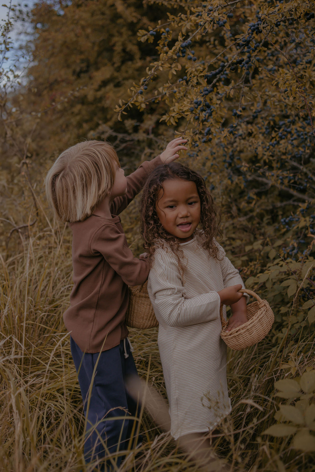 Two children in a natural setting with trees and grass, holding baskets.