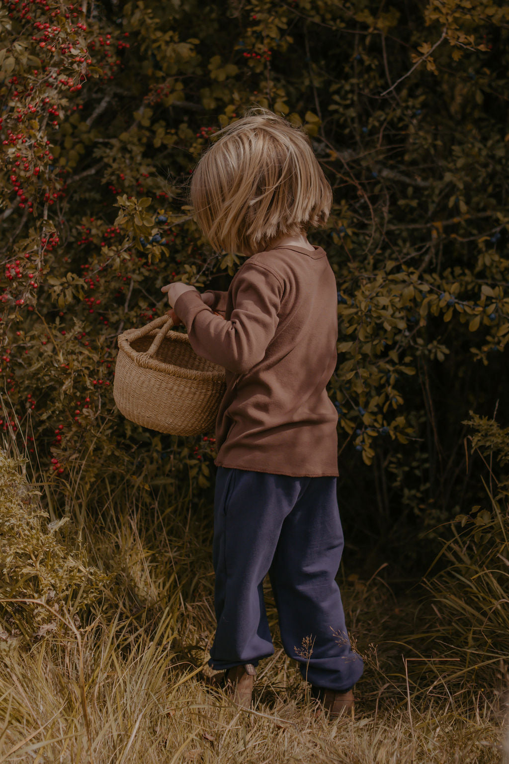 Child holding a woven basket in a natural setting with greenery
