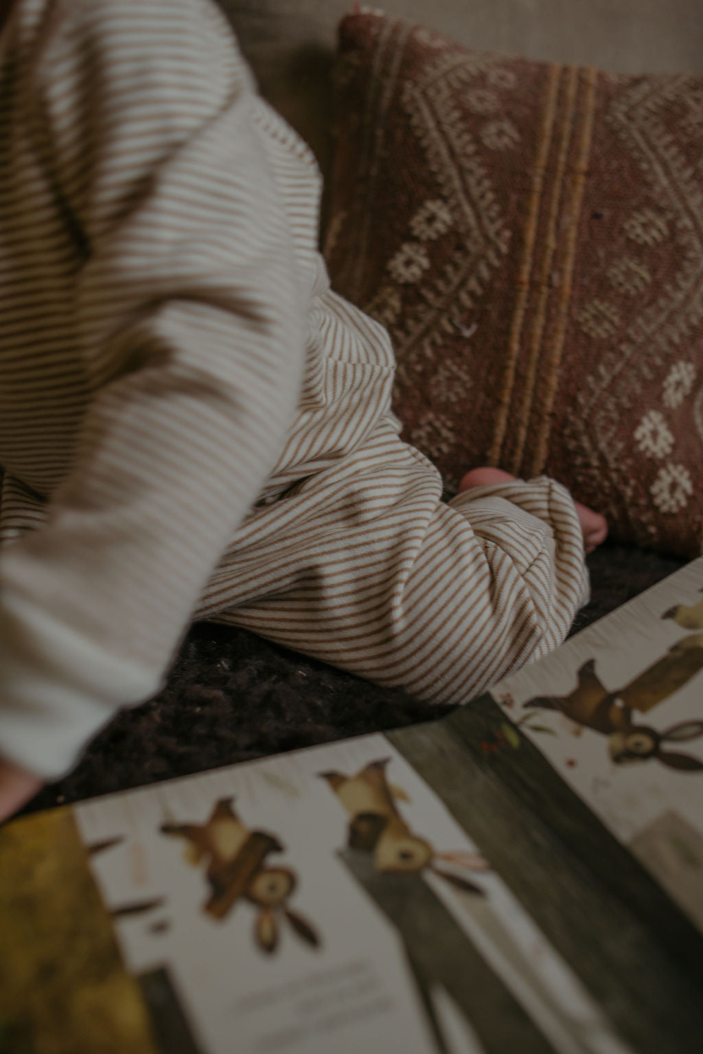 Person in a striped sweater sitting on a couch with a children's book featuring animal illustrations.