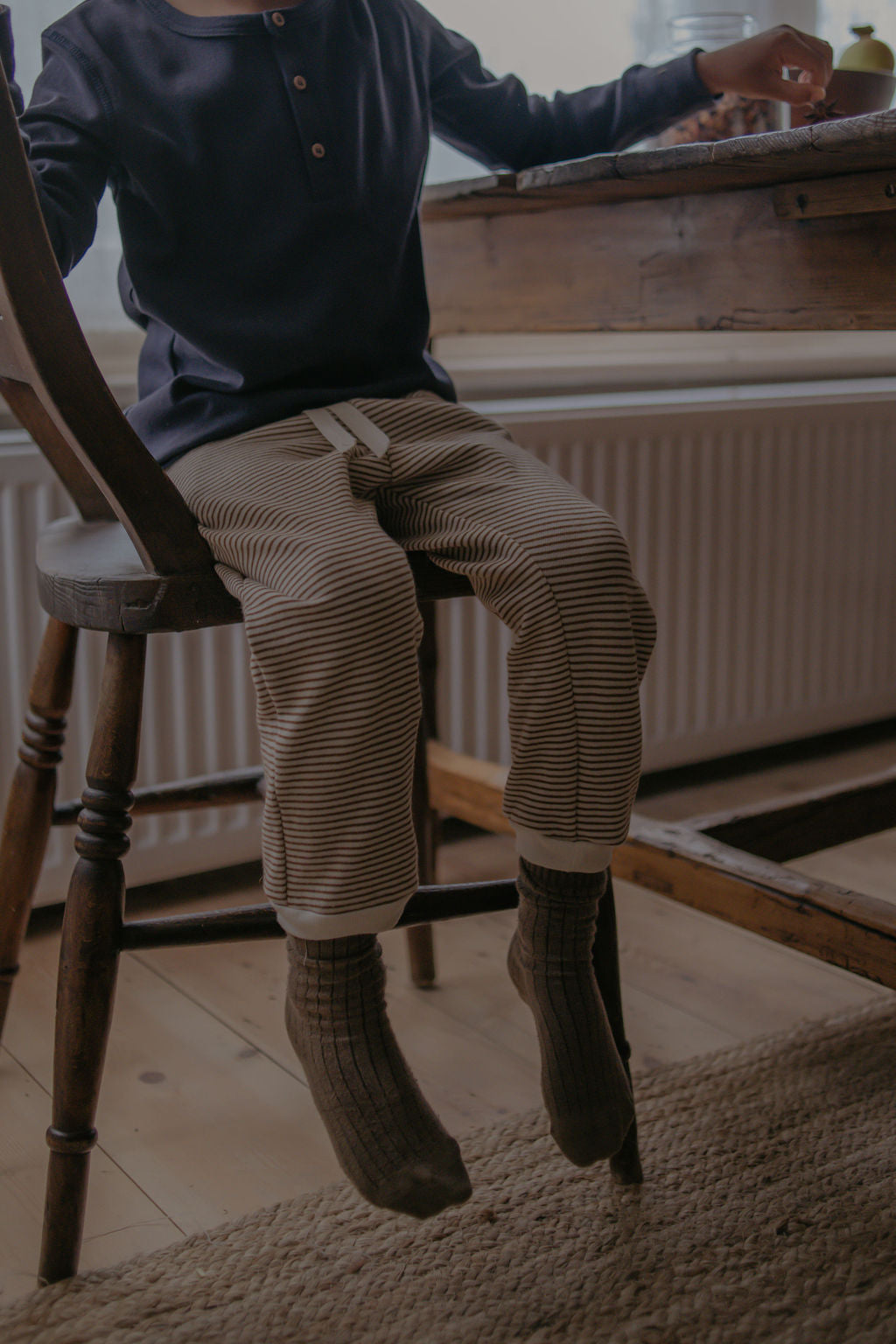 Person sitting on a wooden chair in a room with a radiator and a window.