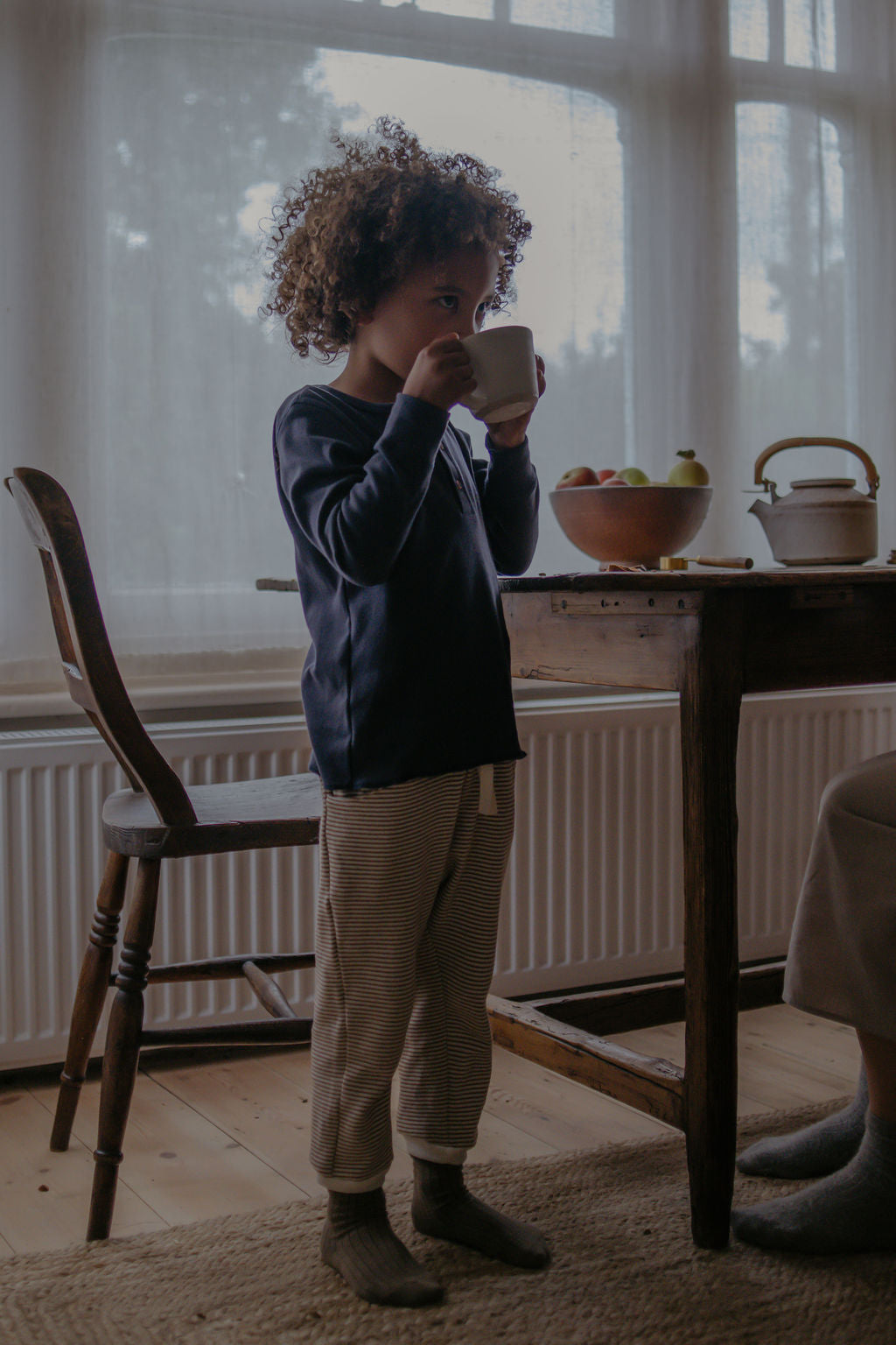 Child drinking from a cup in a room with a table and chairs.