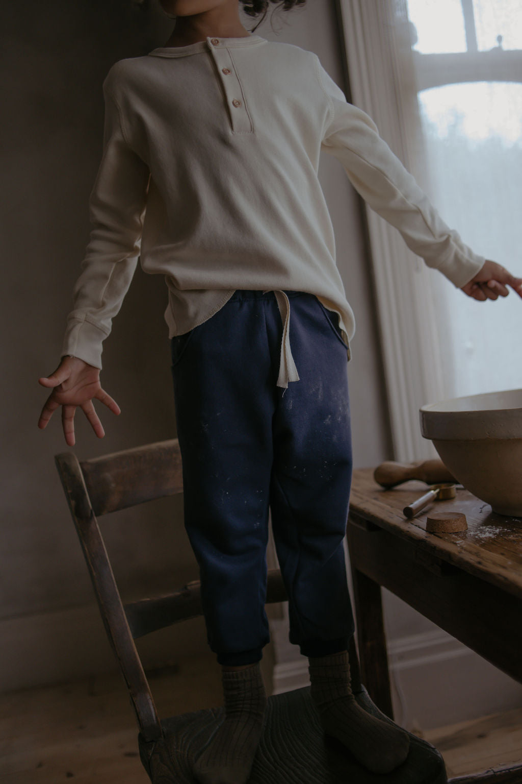 Child standing in a room with a wooden table and various items