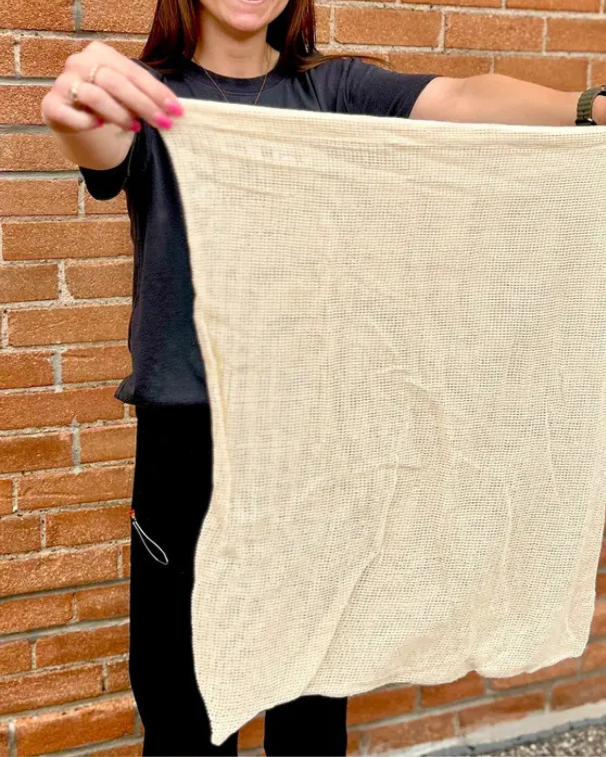 Person holding a beige fabric against a brick wall