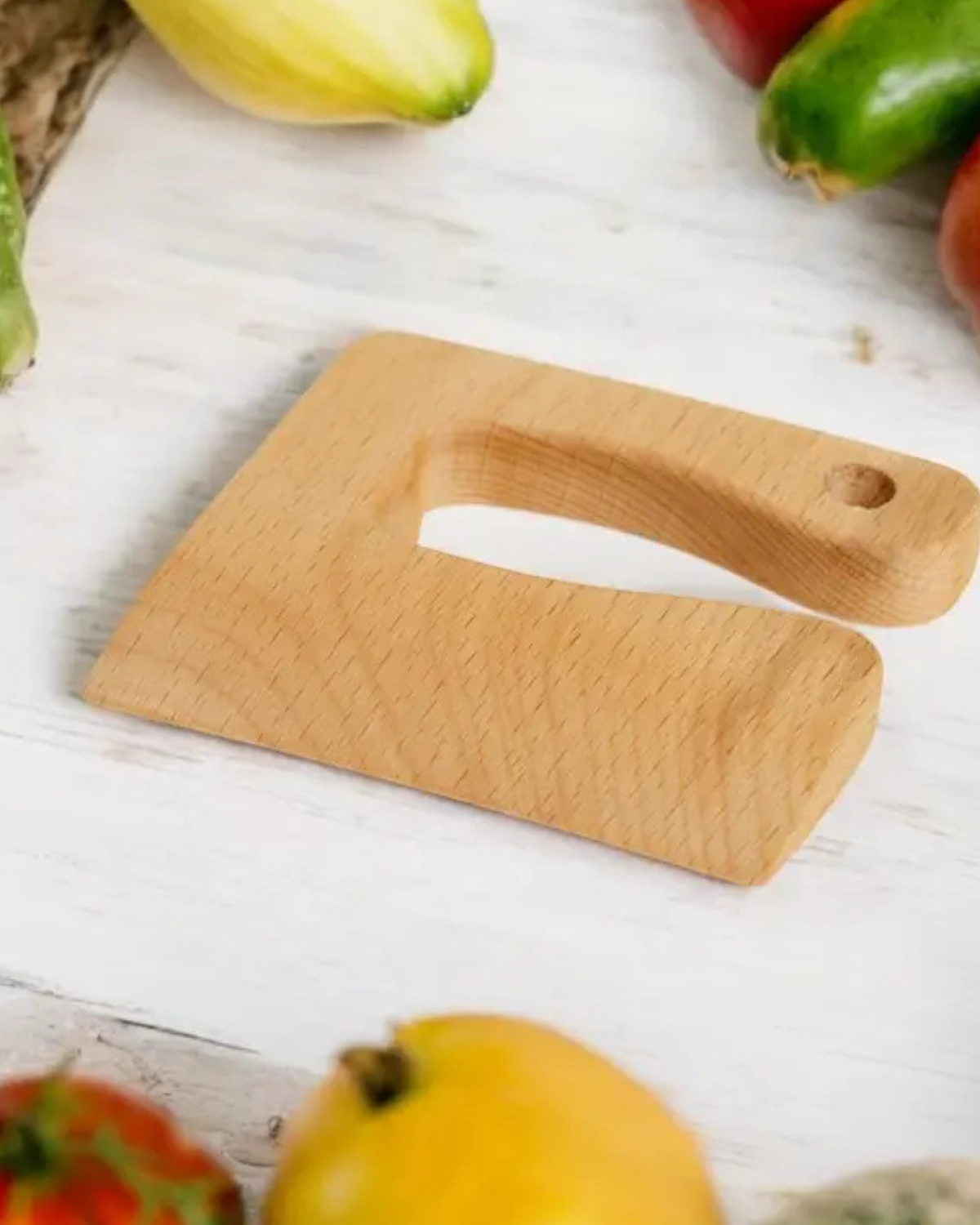 Wooden cutting board with a knife on a white wooden surface with vegetables in the background