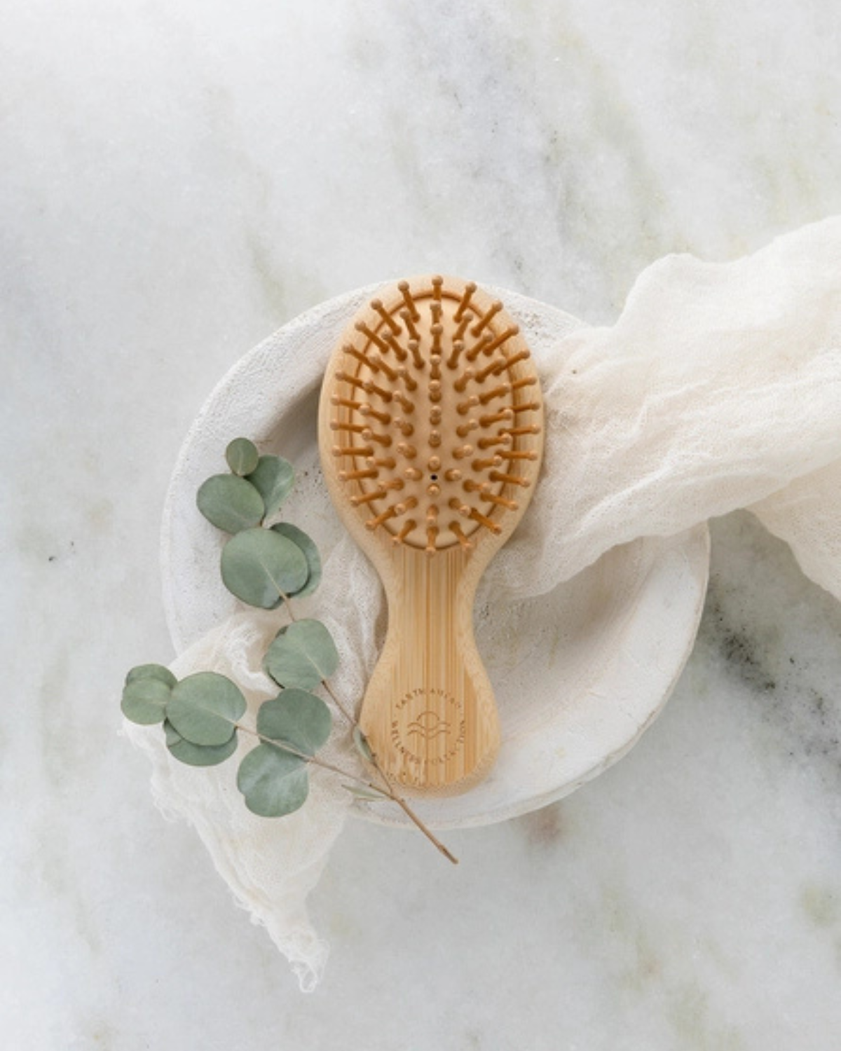 Wooden hairbrush on a white plate with green leaves on a marble surface