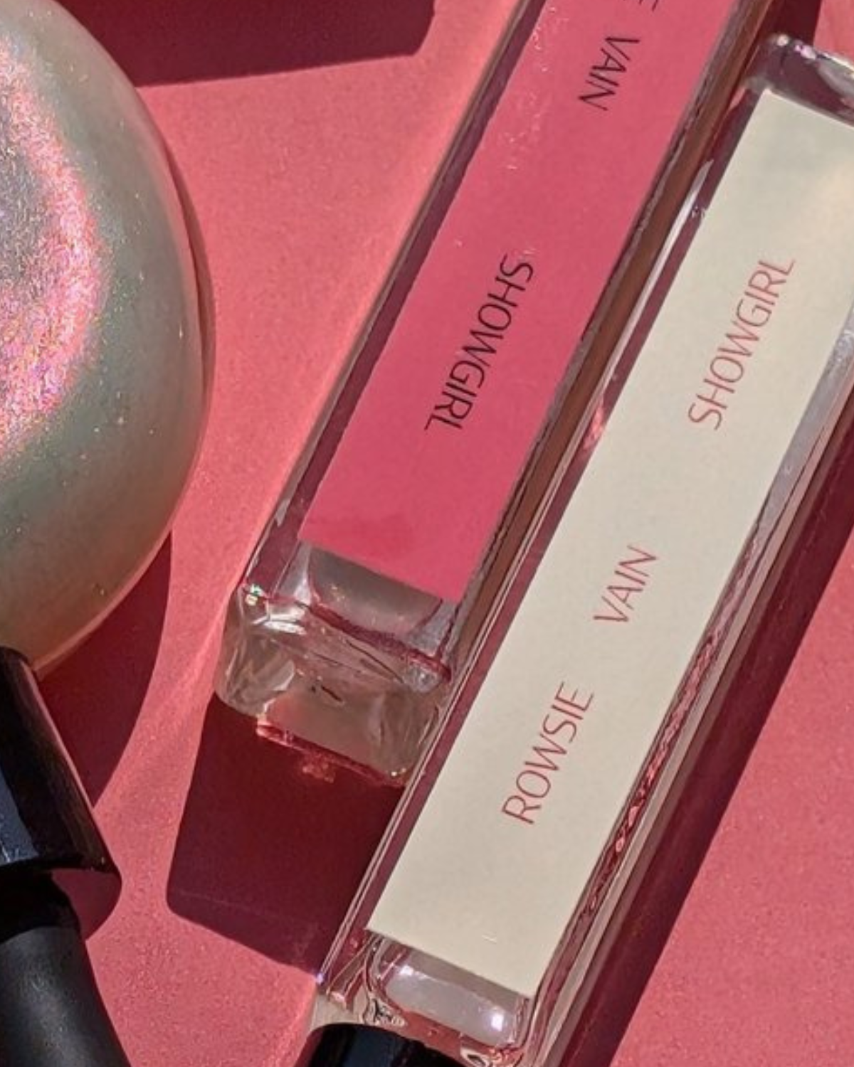 Two perfume bottles labeled 'ROWSIE' and 'VAIN' on a pink background.