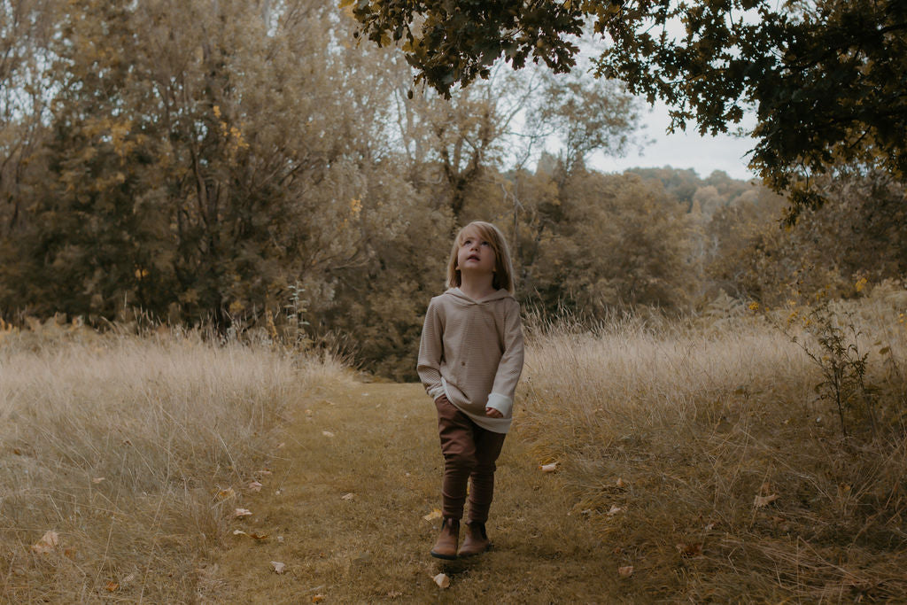 Child walking on a path through a forest with trees and grass in the background
