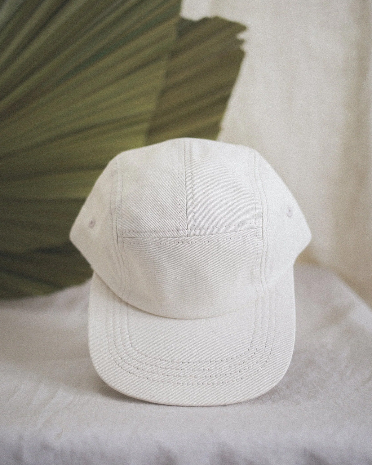 front view of the milky panel hat with palm leaf background